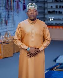 Man wearing a mustard-coloured kanzu with a printed kofia, standing in the Kanzuland shop
