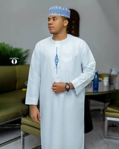 Young man wearing a white kanzu with a blue embroidered collar and a blue patterned kofia